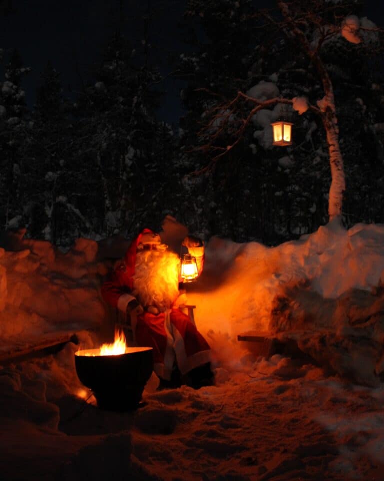 Santa sitting by fire holding lantern in Arctic forest Enontekiö Lapland private Santa experience.