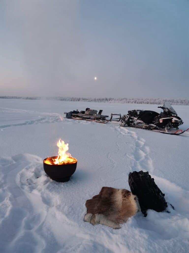A snowmobile and open fire on the ice during ice fishing tour in Enontekiö Lapland.