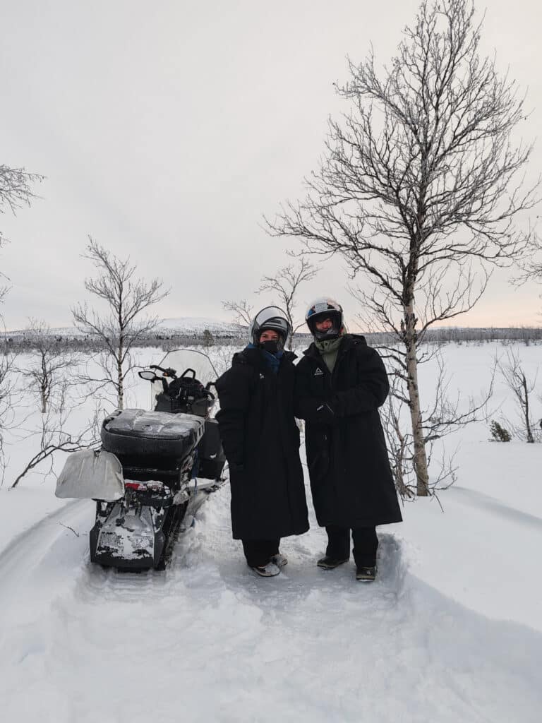 A couple during standing besides a snowmobile during snowmobile safari in Hetta Enontekio Lapland.