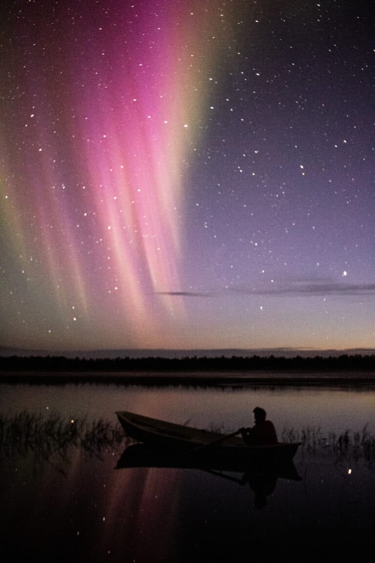 A man canoeing in the lake under the Northern Lights during a tour in Lapland.