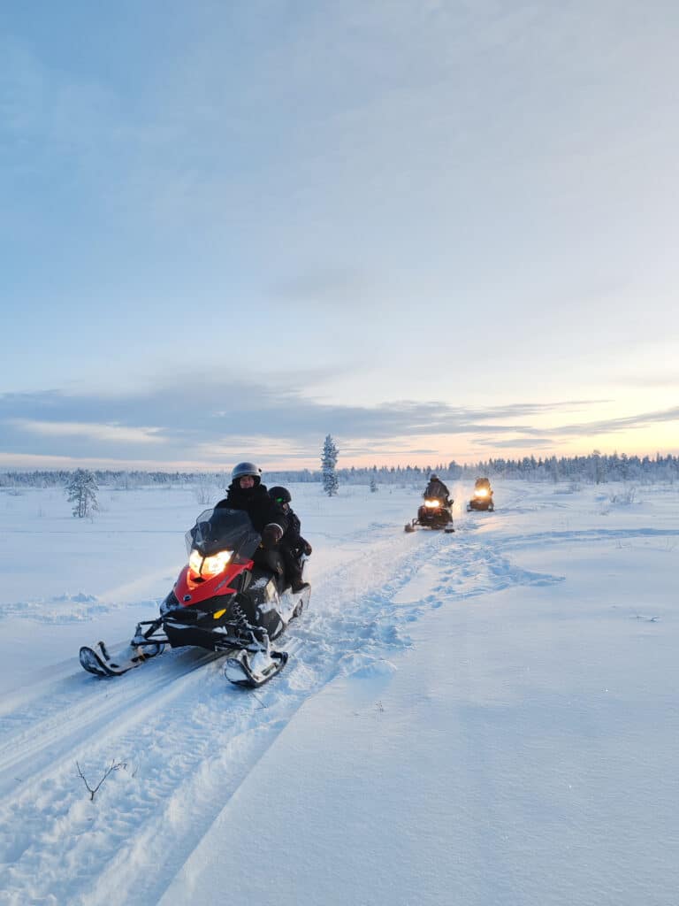 Snowmobile safari Lapland, riders crossing snowy landscape near forest edge, Hetta, Enontekiö during polar night.